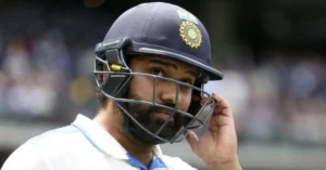 The image features Rohit Sharma, an Indian cricketer, wearing his helmet and looking contemplative during a match. He is seen adjusting his helmet, possibly after a delivery or a close call on the field. The Indian cricket team logo is visible on his helmet.