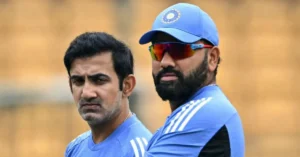 Two Indian cricketers in blue training jerseys, one with a serious expression and the other wearing a cap and reflective sports sunglasses, standing in a stadium.